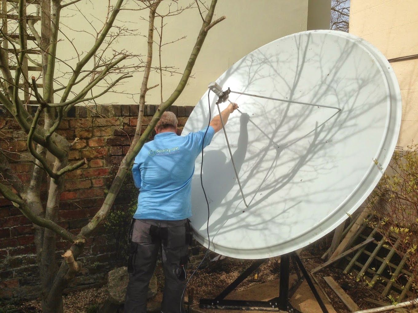 Derek from Sparky-UK aligning a large satellite dish in a garden